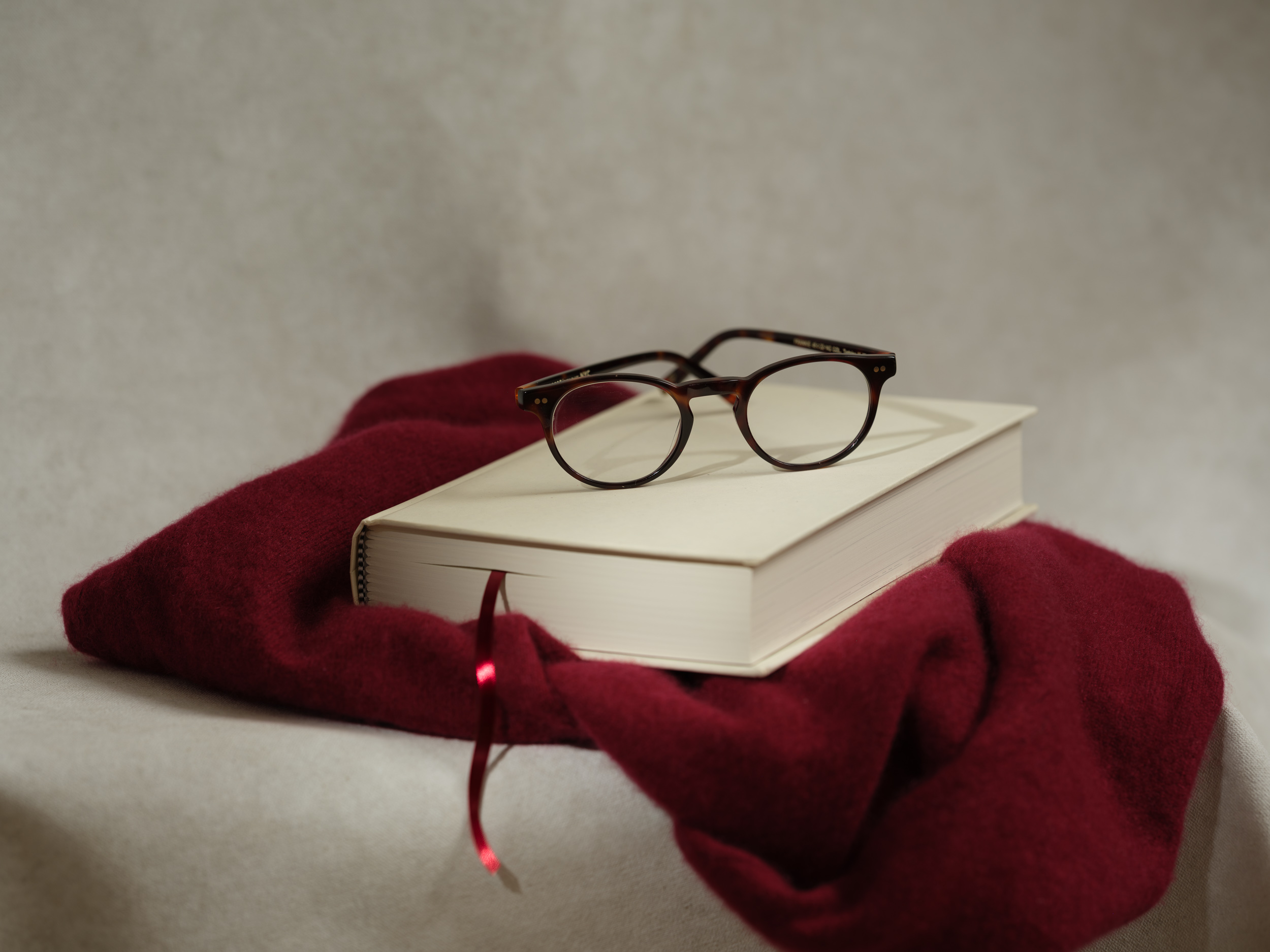 Tortoiseshell reading glasses resting on a closed cream-bound book, on a folded deep-red wool throw